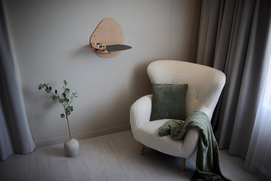 Wall-mounted wooden cat feeding station with two metal bowls and a dark non-slip mat, minimalist design, installed on a light-colored wall near a sofa.