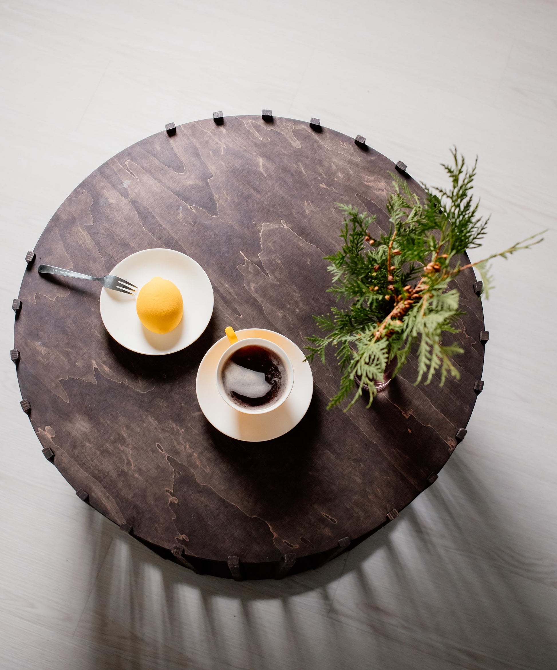 A dark wooden dog house designed to look like a coffee table with a plant on top and two cups of coffee set on it.
