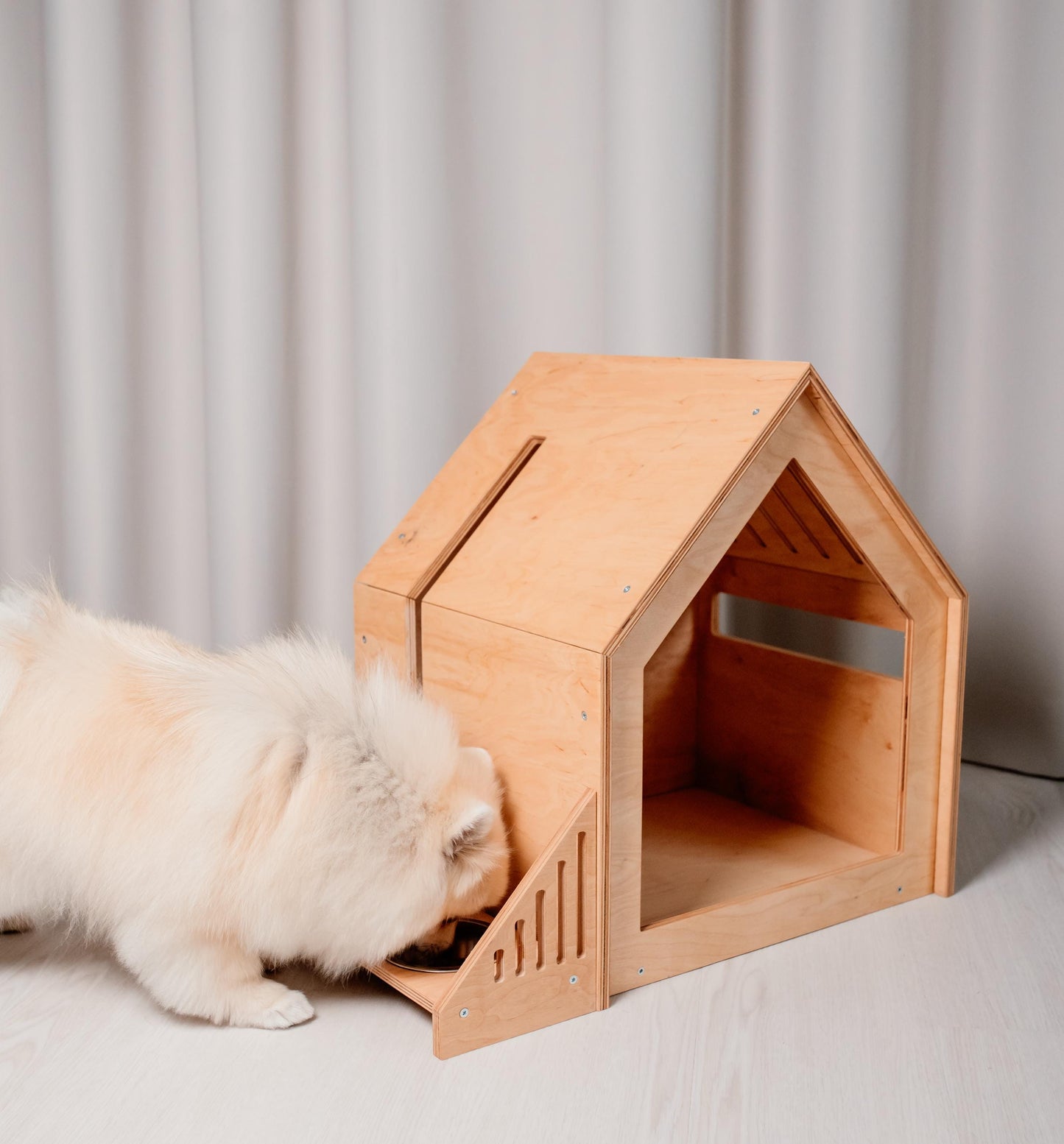 Small dog resting inside modern wooden dog house with feeder set