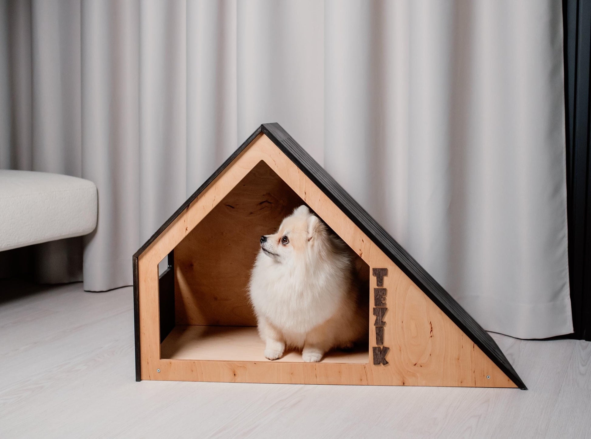 Small dog resting inside modern wooden indoor dog house with personalization