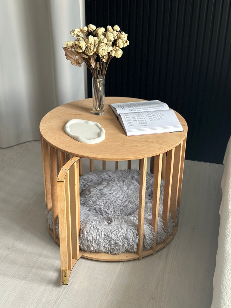 Round wooden side table with a vase of flowers, small round mirror, and book on top.